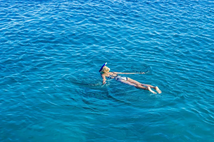 Una persona haciendo snorkel boca abajo en agua azul y transparente, vista desde arriba